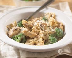 a white bowl filled with pasta and broccoli on top of a wooden table