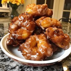 a plate full of glazed donuts on a counter top with flowers in the background