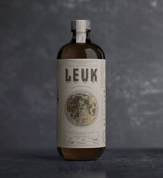 a bottle of liquor sitting on top of a table next to a gray wall with the word leuk printed on it