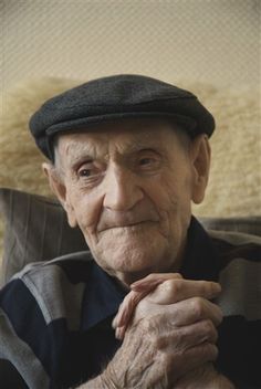 an old man wearing a hat and sitting on a couch with his hands folded up