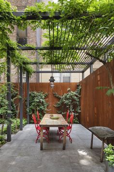 an instagram photo of a table and red chairs in a courtyard with trees on either side