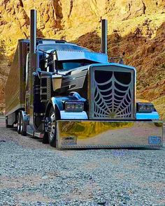 a blue semi truck with a spider web design on the front is parked in gravel