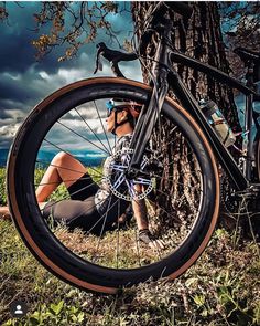 a woman sitting next to a tree with her bike on the ground and looking at it