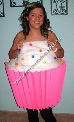 a woman in a pink cupcake costume holding a large white frosted cupcake