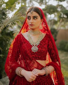 a woman wearing a red bridal outfit with jewelry on her neck and hands in her pockets