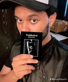 a man holding up a book in front of his face while wearing a baseball cap