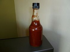 a bottle filled with ketchup sitting on top of a black table next to a white wall