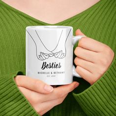 a woman holding a white coffee mug with the words besties written on it in black