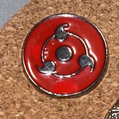 a red and silver button sitting on top of a cork covered table next to a coin