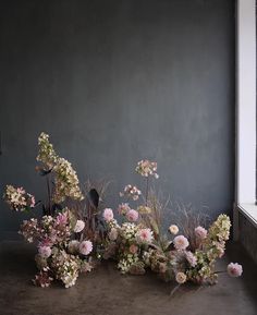 a bunch of flowers sitting in front of a window on the ground next to a wall