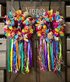 two colorful wreaths hanging on the front door of a store with ribbons attached to them