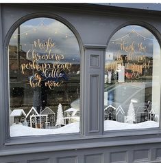 two windows with christmas decorations in them and the reflection of houses on one window is shown