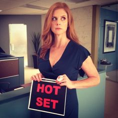 a woman holding a sign that says hot set in an office cubicle with her hands on her hips