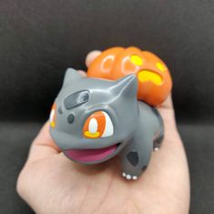 a small toy cat sitting on top of a person's hand next to an orange pumpkin