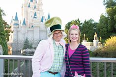 a man and woman standing next to each other in front of a castle at disneyland