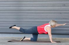 a woman in red shirt doing push ups on a yoga mat with her legs spread out