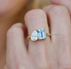 a woman's hand holding an engagement ring with two pear shaped diamonds on it