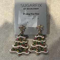 a pair of christmas tree shaped earrings sitting on top of a white table next to a box