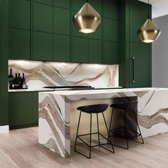 a modern kitchen with green cabinets and marble counter tops, two stools at the bar