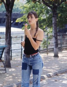 a woman eating an ice cream cone on the sidewalk in front of some trees and benches