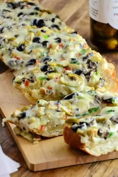 two slices of bread with olives and cheese on a cutting board next to a bottle of wine