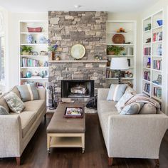 a living room with two couches and a fireplace in the center, surrounded by bookshelves