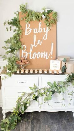 a baby is bloom sign sitting on top of a dresser with greenery around it