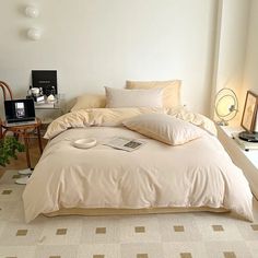 a bed with white sheets and pillows in a room next to a table filled with plants