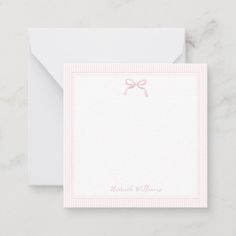 a white card with pink ribbon and bow on the front, next to an envelope