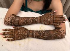 two women with henna tattoos on their hands and arms, sitting in front of a table