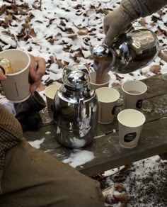 two people are sitting at a picnic table with cups and kettles