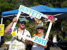 a man and woman holding up signs under a blue tent at a fair with flowers on them