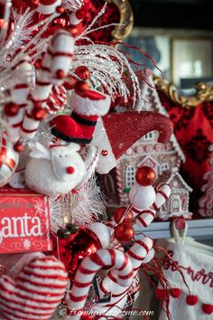 red and white christmas ornaments hanging from a tree in front of a house with santa's hat on it