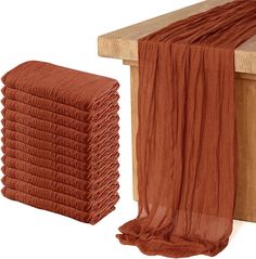 a stack of orange towels sitting on top of a wooden bench next to a pile of red scarves