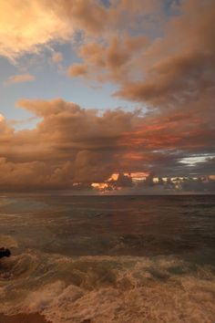 the sun is setting over the ocean with clouds in the sky and waves crashing on the shore