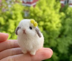 a tiny stuffed animal is held in the palm of someone's hand, with trees in the background