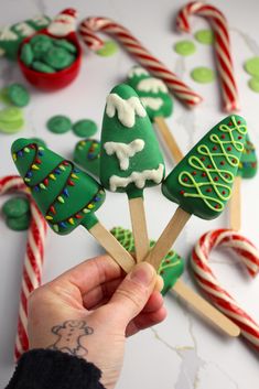 a person is holding up some green and white candy canes with trees on them