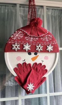 a snowman ornament hanging on the side of a window with mittens and gloves