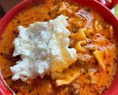 a red bowl filled with pasta and cheese covered in gravy on top of a table