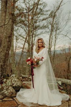 a woman in a wedding dress holding a bouquet and standing next to a large tree