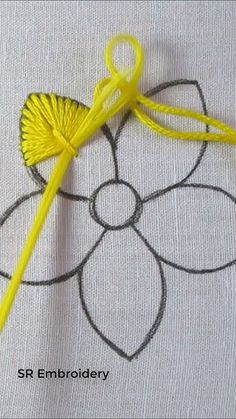 a yellow crochet hook is laying on a piece of white fabric next to a flower