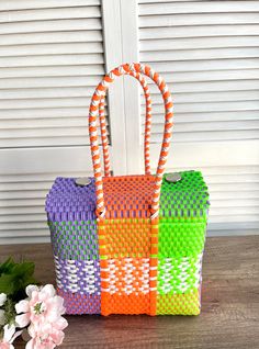 two woven bags sitting on top of a wooden table next to flowers and a window