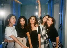 four young women posing for the camera in front of a blue glass wall with their arms up