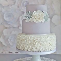 a three tiered cake with white flowers on the top and grey frosting on the bottom