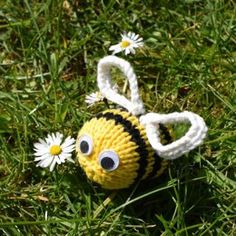 a yellow and black knitted bee toy laying in the grass with daisies around it