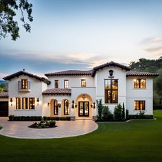 a large white house with lots of windows and lights on it's front porch