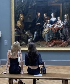 two women sitting on benches in front of a painting with people looking at it and writing