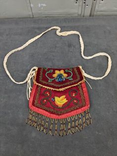 a red purse with tassels hanging from it's side on the ground