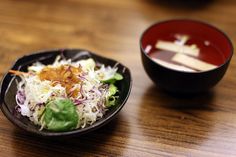 a black plate topped with coleslaw next to a bowl filled with dressing sauce