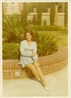 an old photo of a woman sitting on a brick wall in front of some bushes